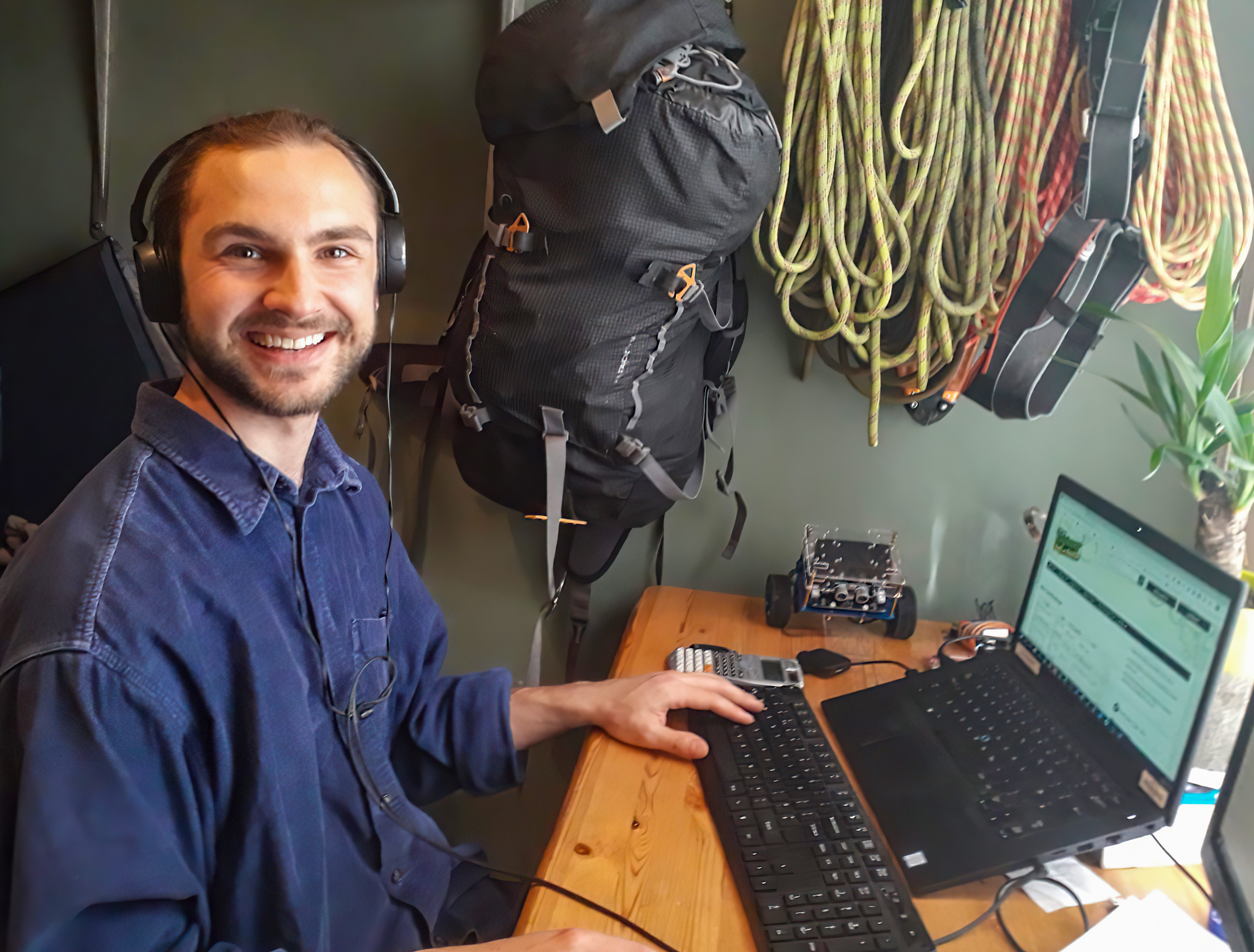 man with headphones on at laptop, smiling to the camera
