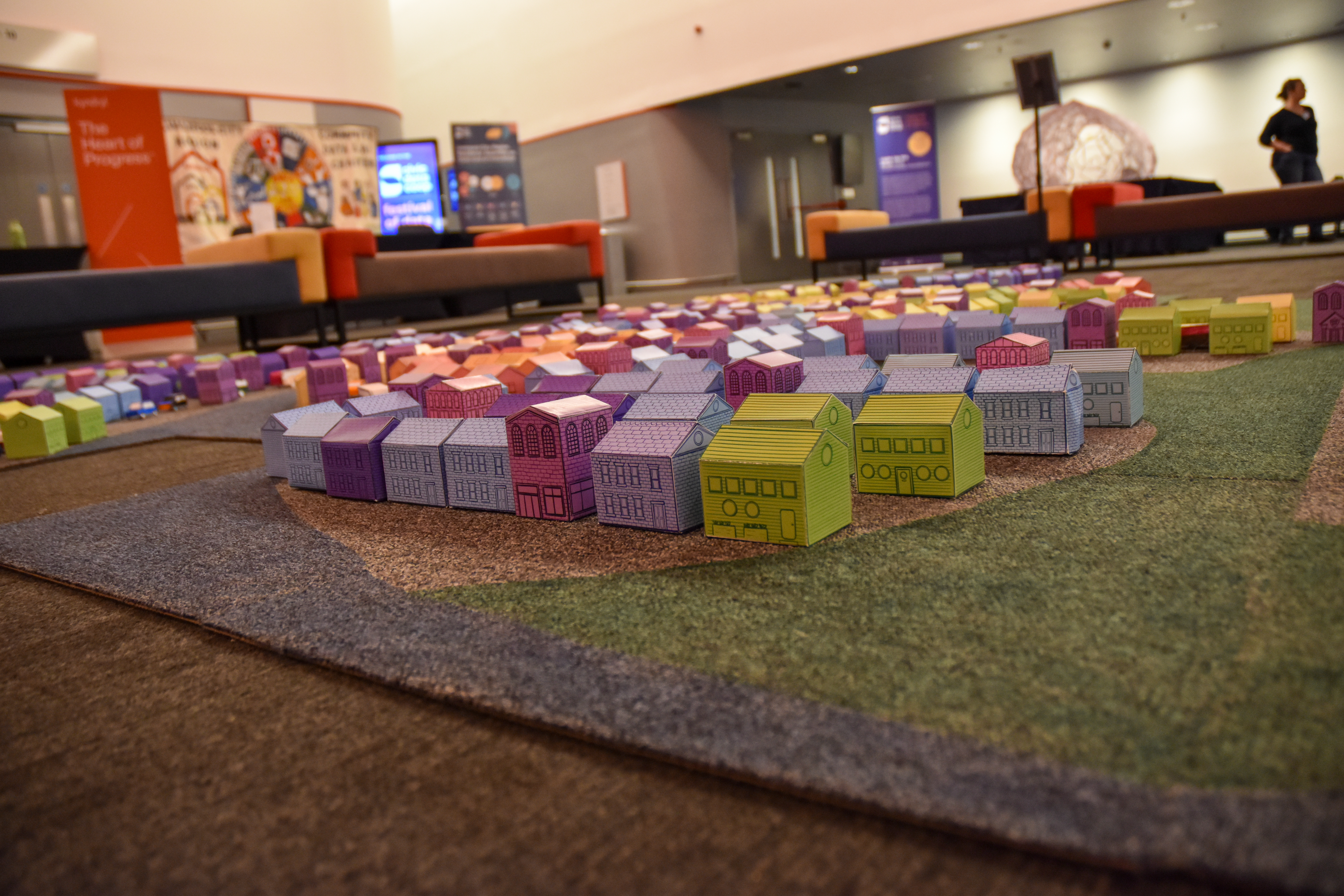 a cardboard colourful village of houses made by children laid on a carpet