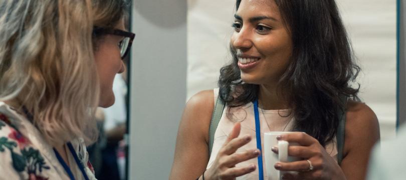 two women talking together, one holding a hot drink