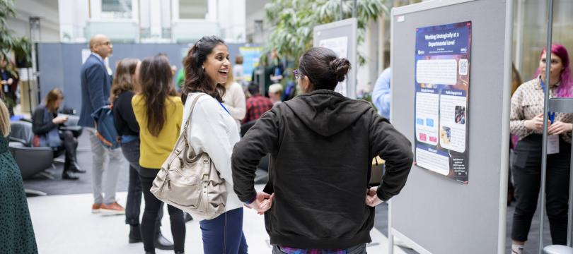 people talking to each other at an event in front of posters with others doing the same in the background