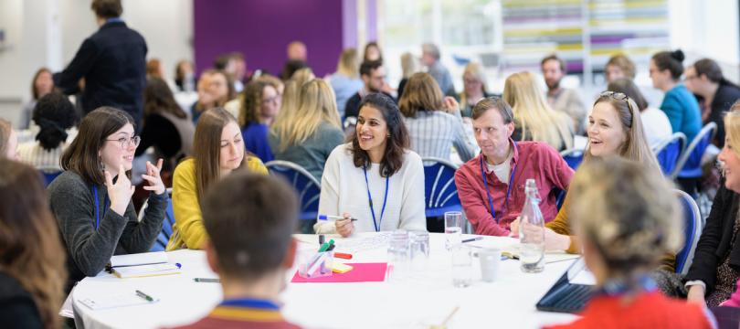 group talking and laughing at roundtable at Engage Live 2022 with many other groups in the background