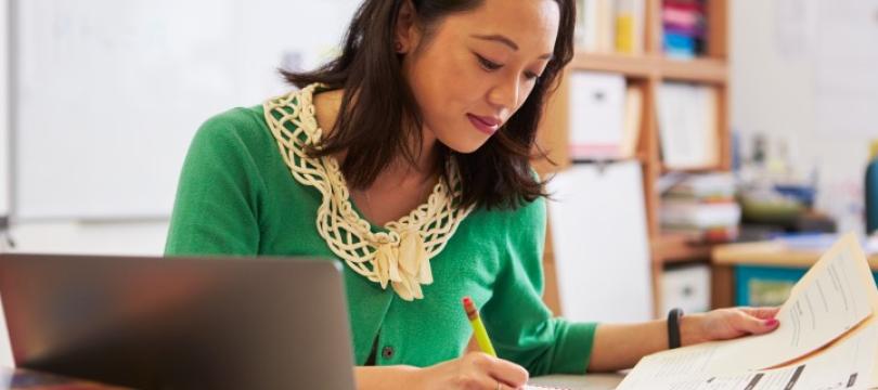 woman hand writing on form with laptop on table next to her