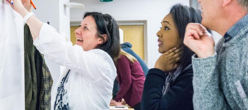 People at a workshop looking up at some notes on the wall and smiling