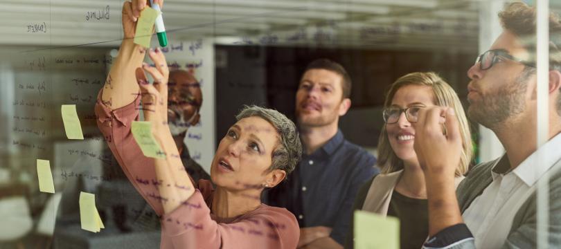 A group of 5 people using post-it notes on a wall to plan