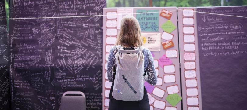 A woman stands in front of a board covered in post-it notes