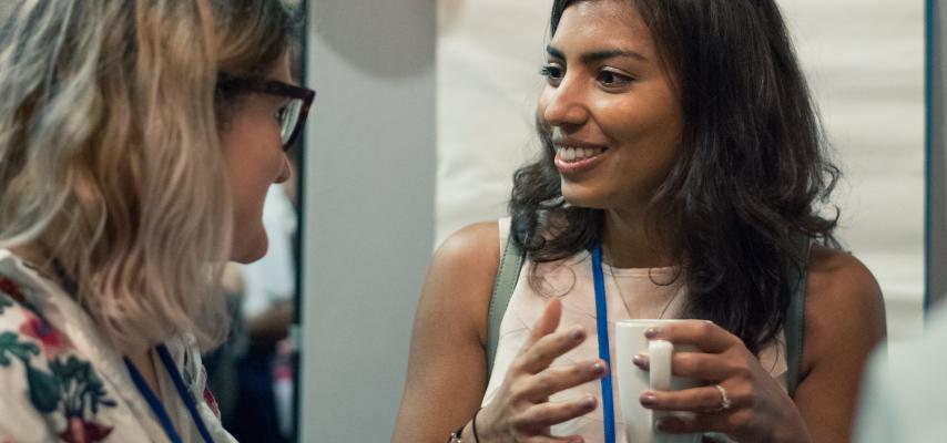 two women talking together, one holding a hot drink