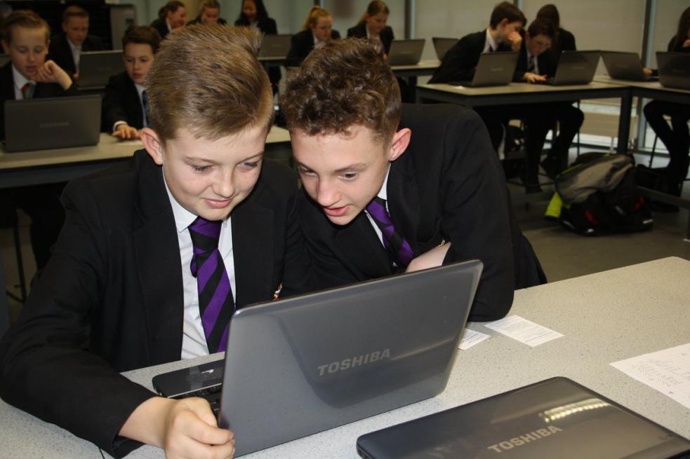 two young people in school uniform looking at a laptop