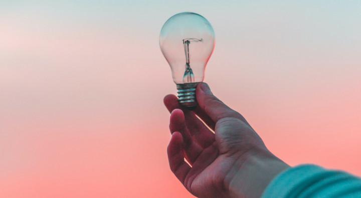 Hand holding on to lightbulb against orange-tinted sky