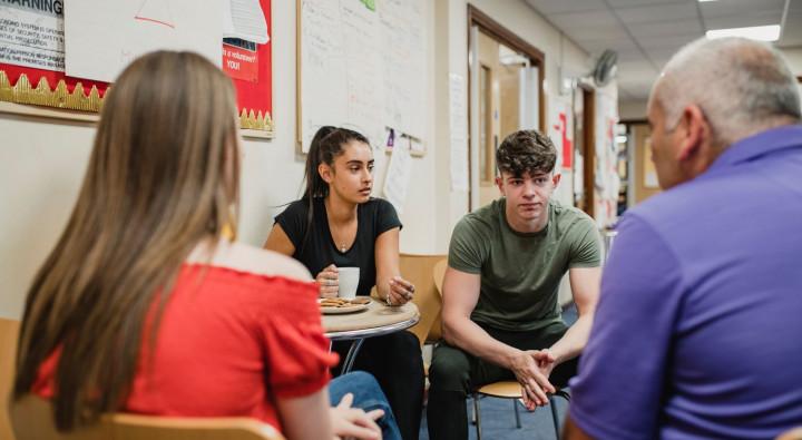 Group of 3 young people and older person speaking together 