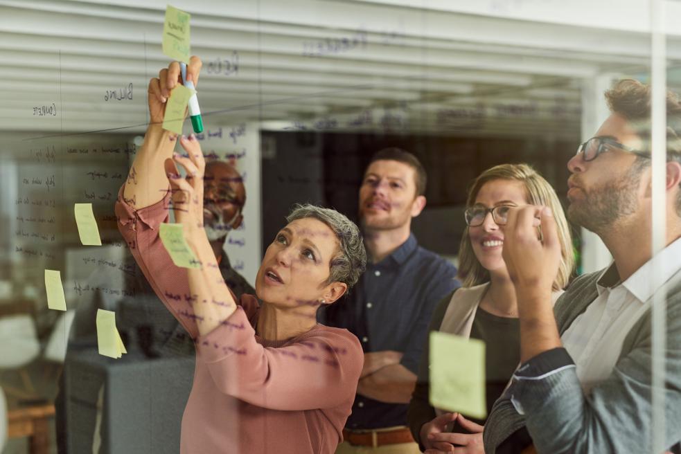 A group of 5 people using post-it notes on a wall to plan
