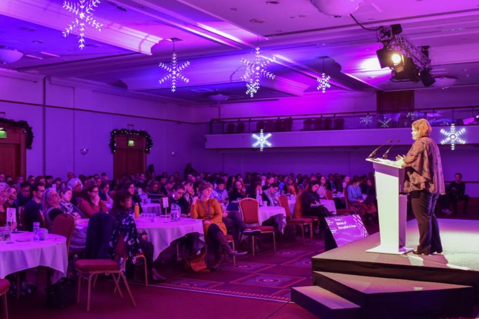 A woman stands on stage presenting to an auditorium of delegates