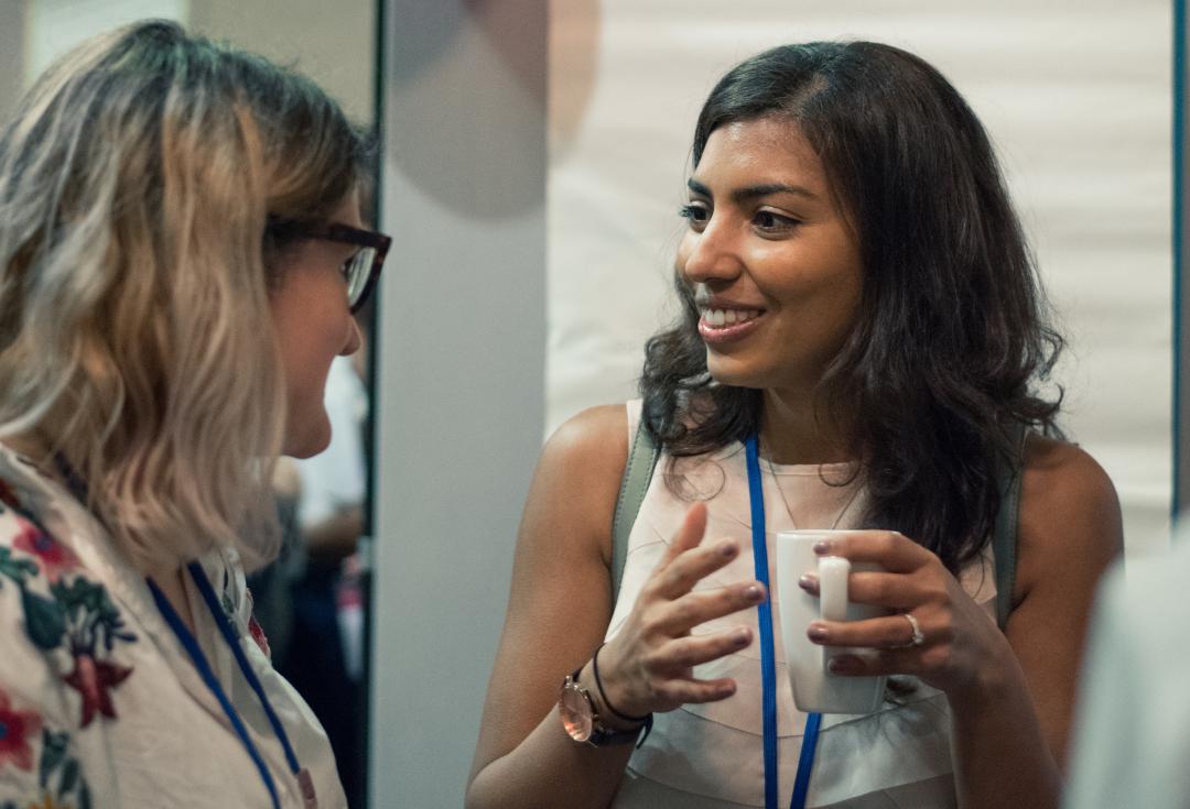 two women talking together, one holding a hot drink