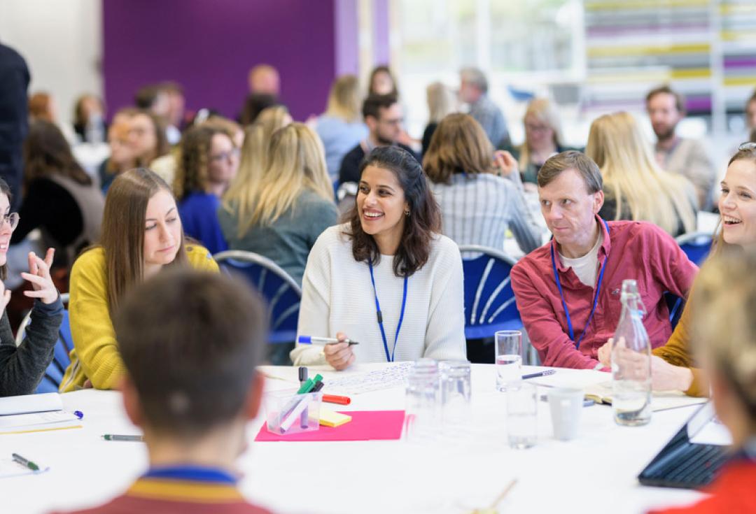 group talking and laughing at roundtable at Engage Live 2022 with many other groups in the background