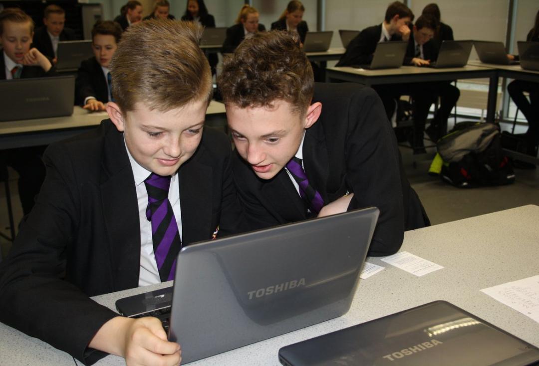 two young people in school uniform looking at a laptop