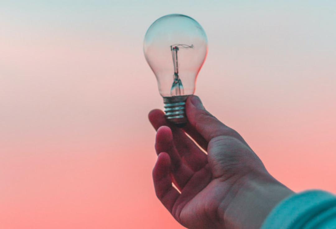 Hand holding on to lightbulb against orange-tinted sky