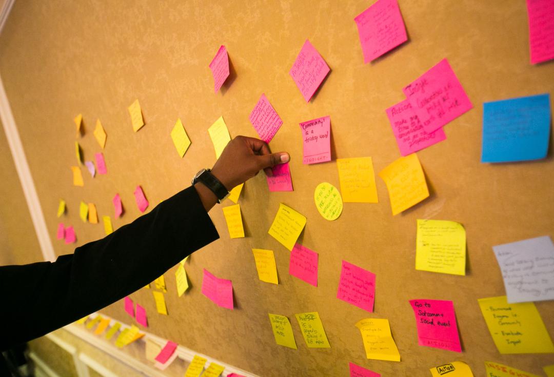 A hand reaching out to put a post-it note on a wall with other post-it notes on
