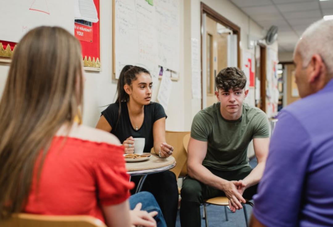 Group of 3 young people and older person speaking together 