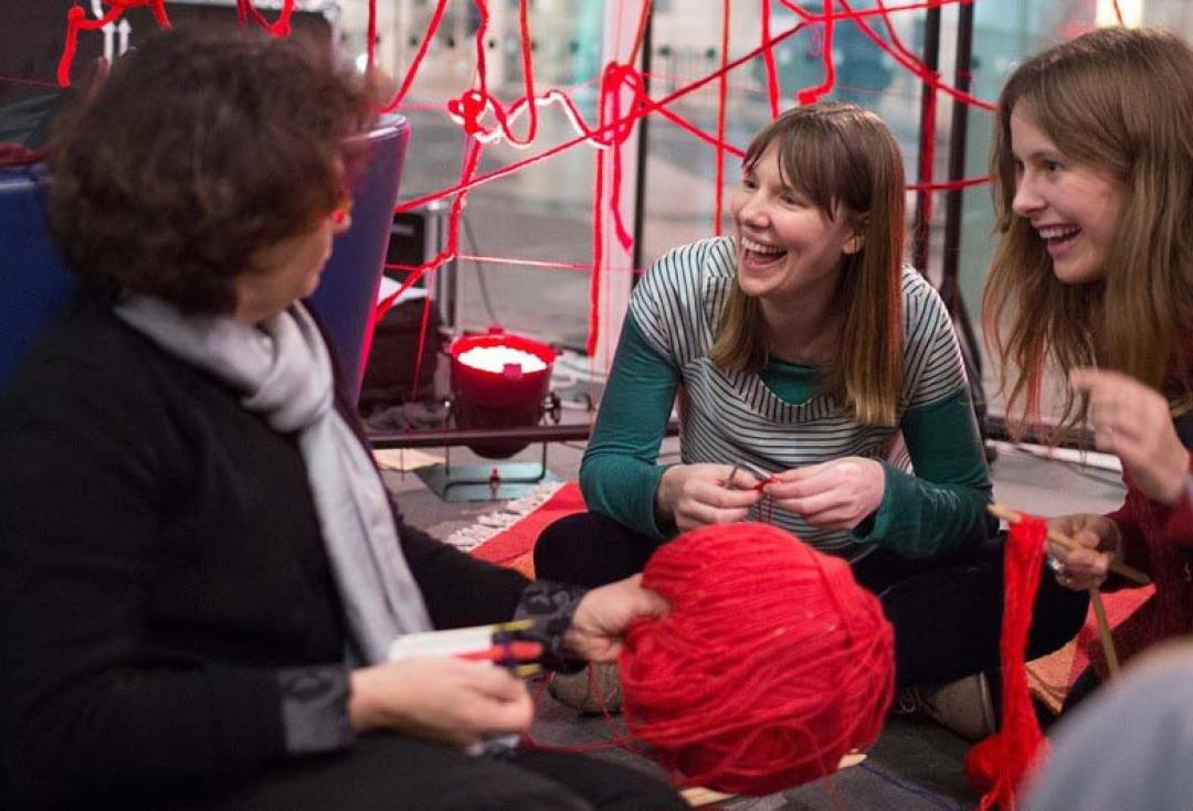 Three women laughing together while taking part in a knitting activity