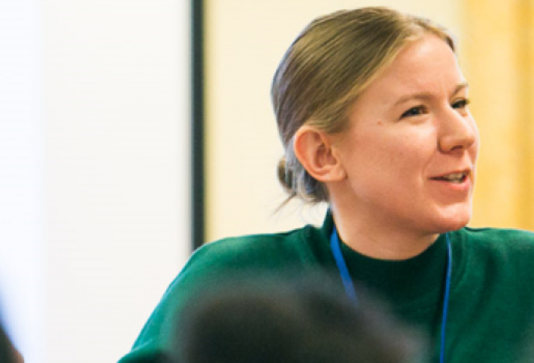 A woman with blonde hair smiling as she speaks to an audience