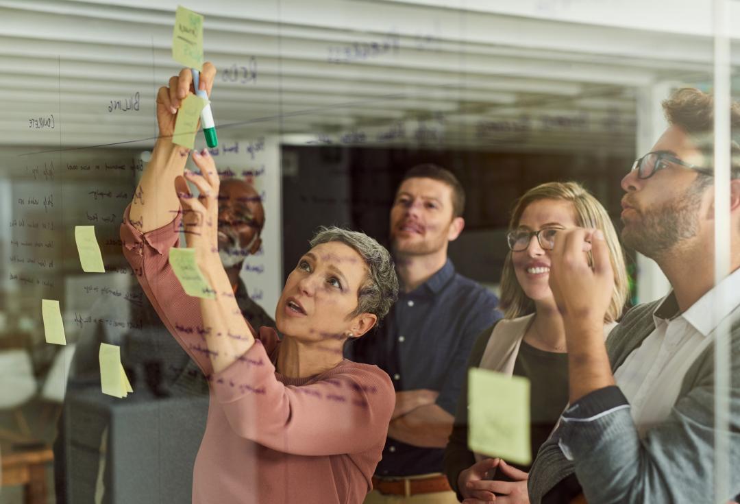 A group of 5 people using post-it notes on a wall to plan