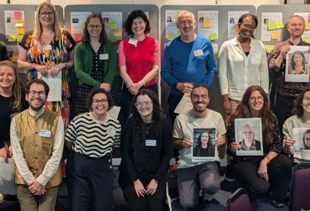 The Academy 2023_24 cohort standing/kneeling in two rows, some holding images of those not in the room