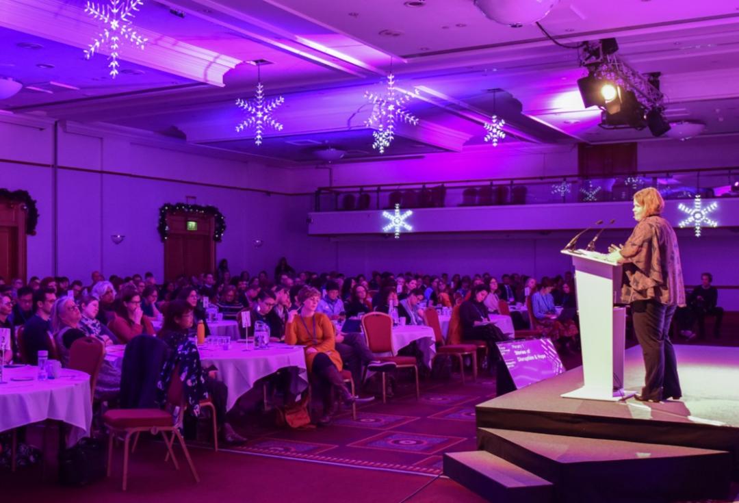 A woman stands on stage presenting to an auditorium of delegates
