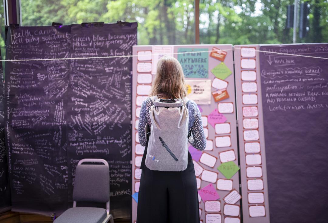 A woman stands in front of a board covered in post-it notes