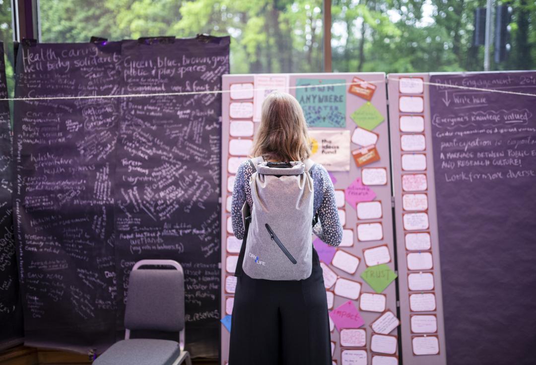 A woman stands in front of a board covered in post-it notes