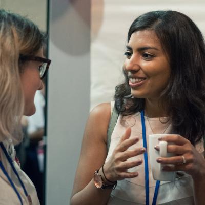 two women talking together, one holding a hot drink