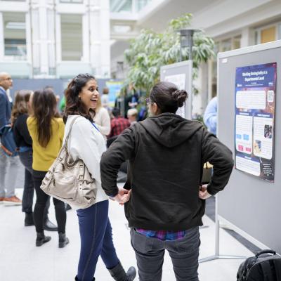 people talking to each other at an event in front of posters with others doing the same in the background