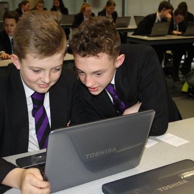 two young people in school uniform looking at a laptop