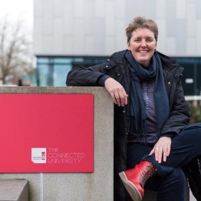 Penny sat on a wall outside a university, smiling 