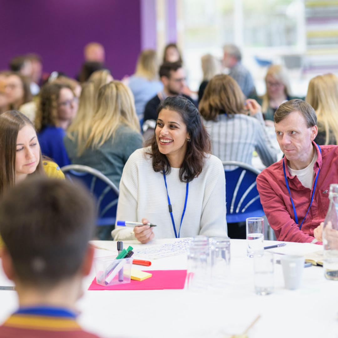 group talking and laughing at roundtable at Engage Live 2022 with many other groups in the background