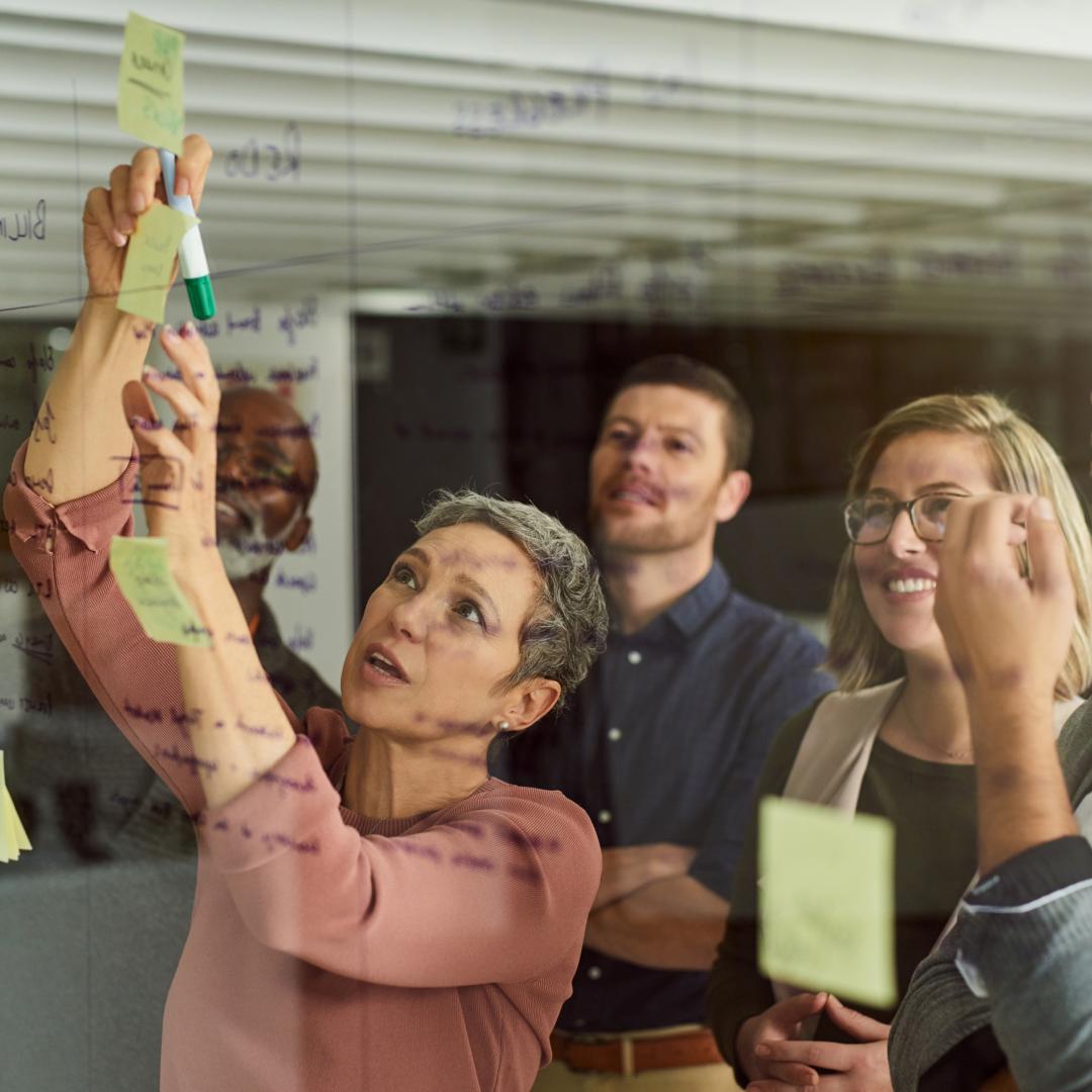 A group of 5 people using post-it notes on a wall to plan