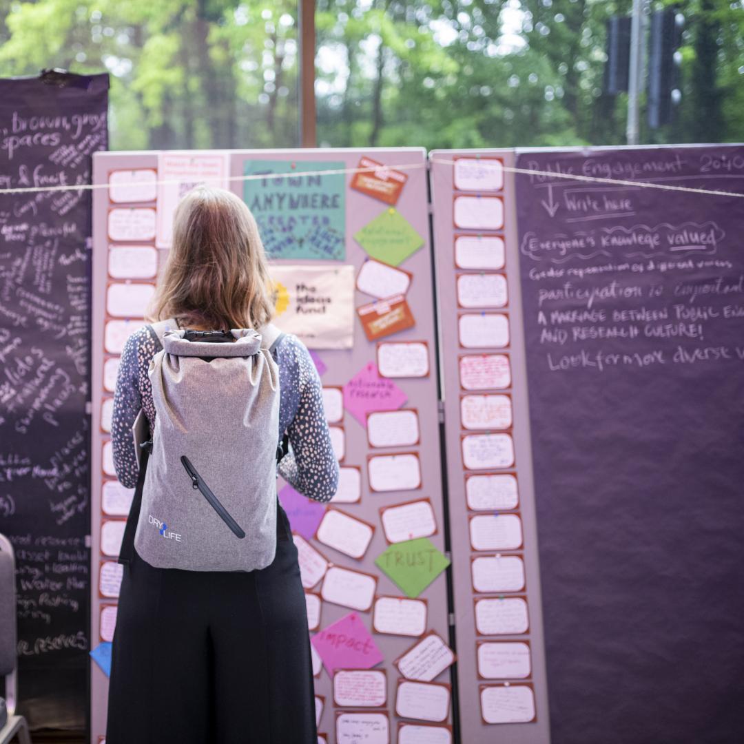 A woman stands in front of a board covered in post-it notes